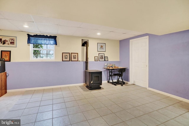 basement with a wood stove, a drop ceiling, and light tile patterned floors