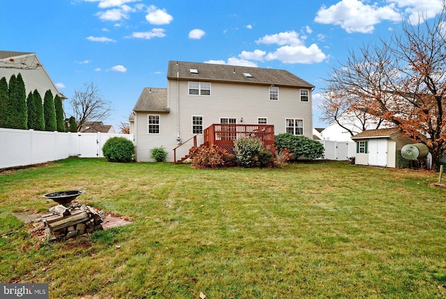 back of property with a wooden deck, a yard, a storage shed, and a fire pit