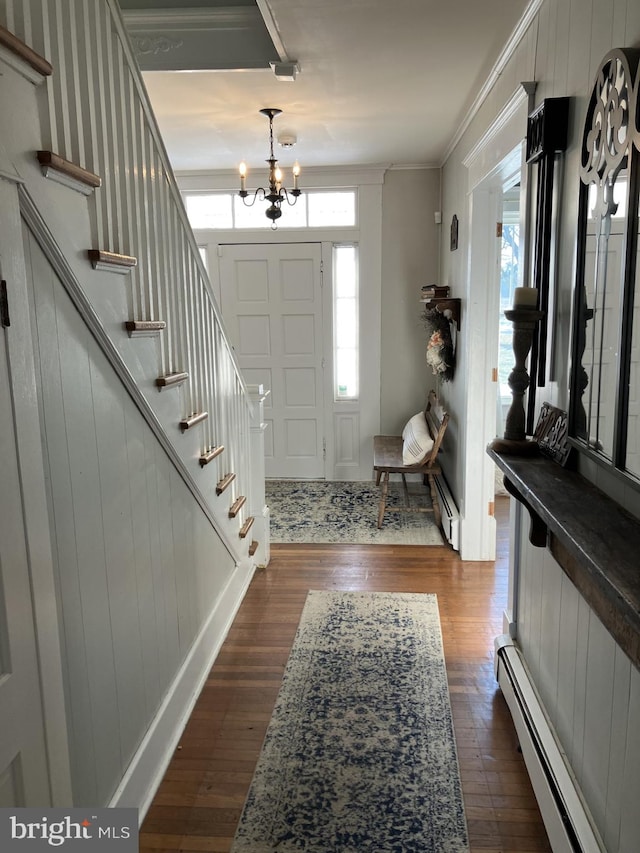 entrance foyer with a baseboard heating unit, dark wood-type flooring, crown molding, and a chandelier