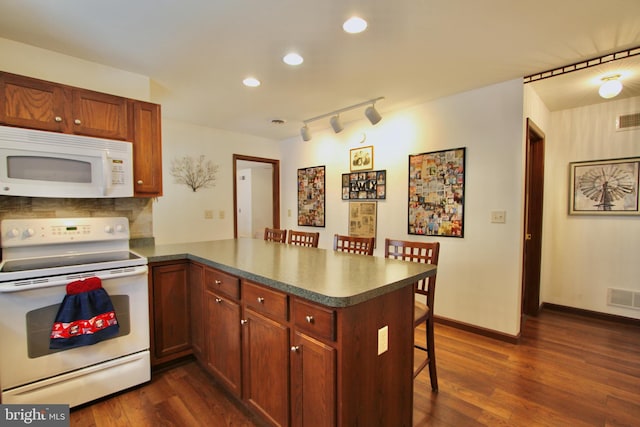 kitchen featuring white appliances, a kitchen breakfast bar, dark hardwood / wood-style floors, tasteful backsplash, and kitchen peninsula