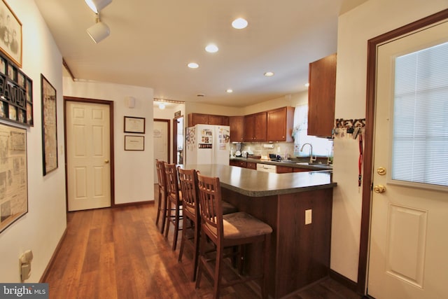 kitchen with white appliances, sink, decorative backsplash, dark hardwood / wood-style floors, and a breakfast bar area