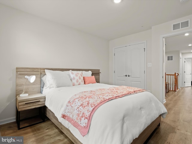 bedroom with wood finished floors, visible vents, a closet, and baseboards