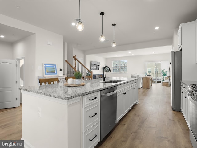 kitchen with an island with sink, light wood-style flooring, appliances with stainless steel finishes, white cabinetry, and a sink