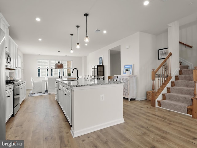 kitchen featuring a center island with sink, a sink, stainless steel appliances, white cabinets, and light wood finished floors