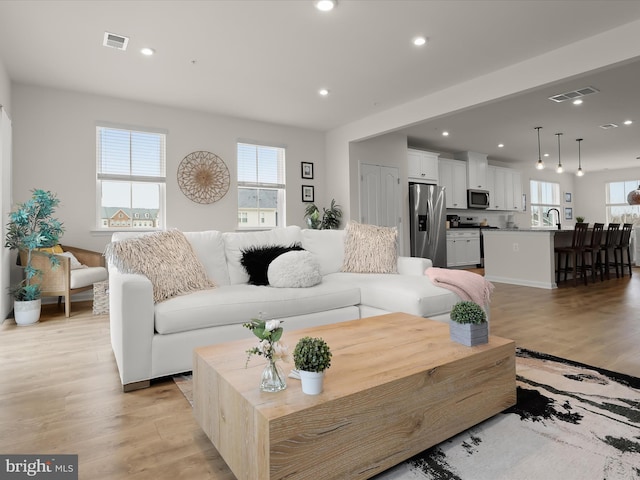 living room with light wood-style flooring, a healthy amount of sunlight, and visible vents