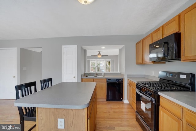 kitchen featuring ceiling fan, a center island, sink, a breakfast bar, and black appliances