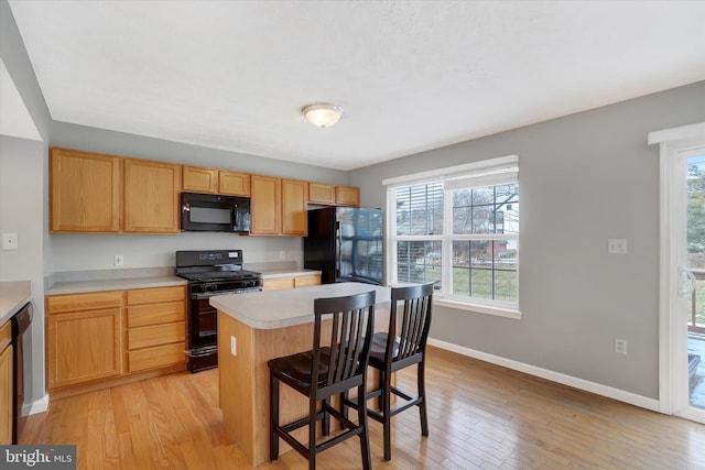 kitchen featuring black appliances, a kitchen island, a kitchen bar, and light hardwood / wood-style floors