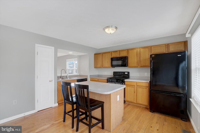 kitchen with black appliances, sink, light wood-type flooring, a kitchen island, and a kitchen bar