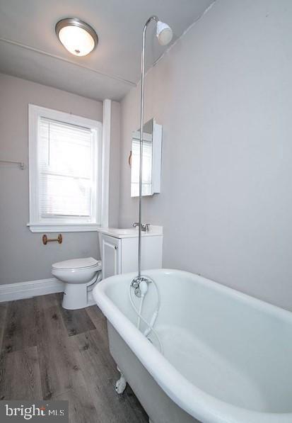 bathroom with a bathing tub, toilet, and wood-type flooring