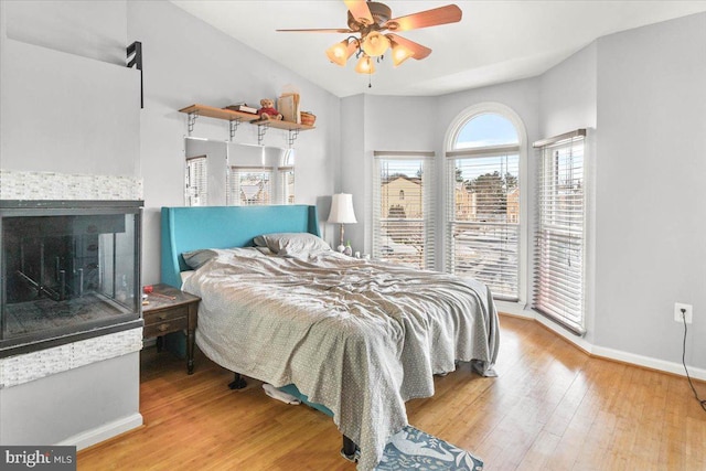 bedroom with a tile fireplace, hardwood / wood-style flooring, and ceiling fan