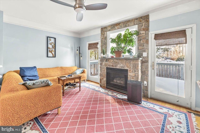 living room featuring ceiling fan, crown molding, and a fireplace