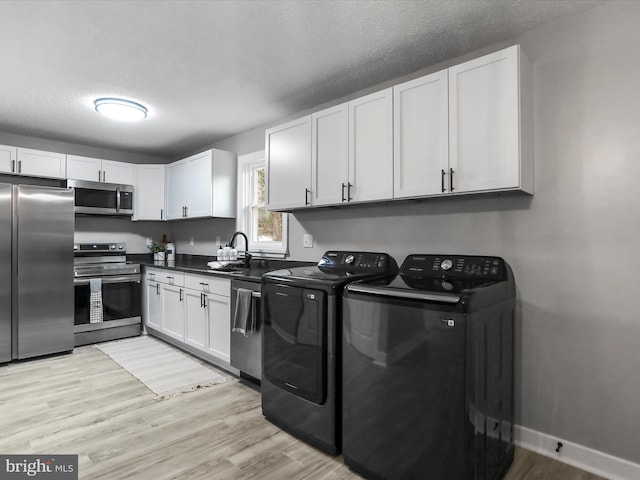 clothes washing area with light hardwood / wood-style floors, sink, washing machine and clothes dryer, and a textured ceiling