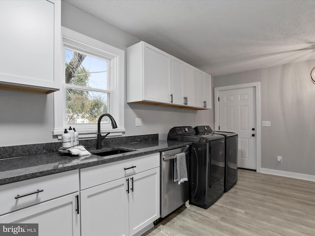 clothes washing area featuring sink, washing machine and clothes dryer, light hardwood / wood-style flooring, a textured ceiling, and cabinets