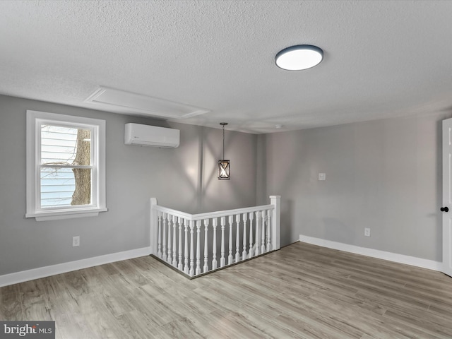 spare room with a wall unit AC, a textured ceiling, and wood-type flooring