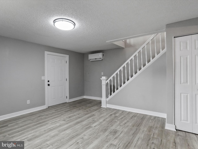 interior space with a textured ceiling, a wall mounted AC, and light hardwood / wood-style floors