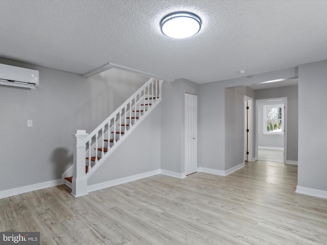 basement featuring a textured ceiling, a wall mounted AC, and light hardwood / wood-style flooring