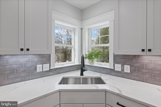 kitchen featuring decorative backsplash, light stone countertops, sink, and white cabinetry