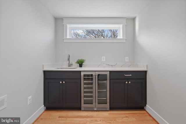 bar with light stone counters, sink, beverage cooler, and light wood-type flooring