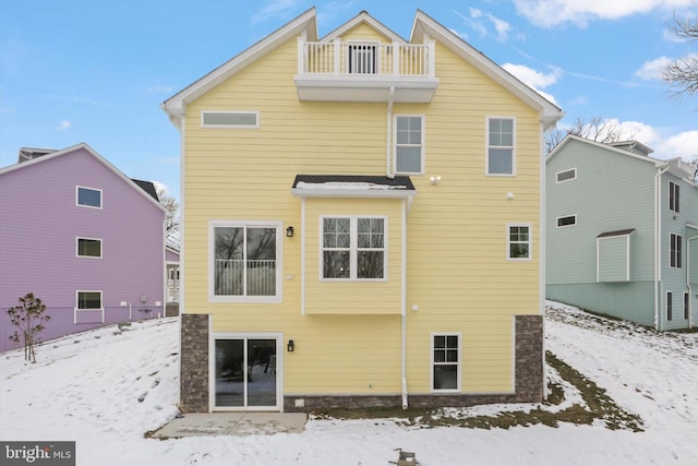 snow covered back of property with a balcony