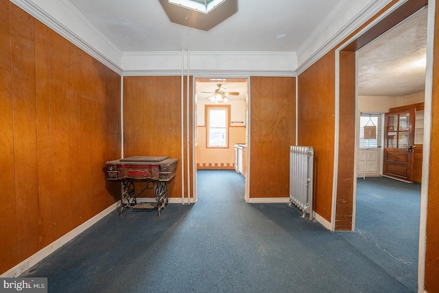 corridor with radiator, dark carpet, wood walls, and ornamental molding