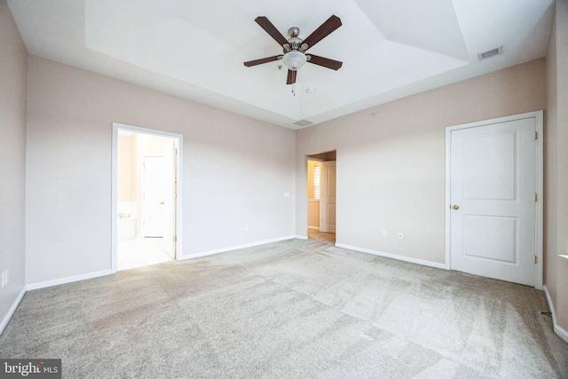 spare room with a raised ceiling, light carpet, and ceiling fan