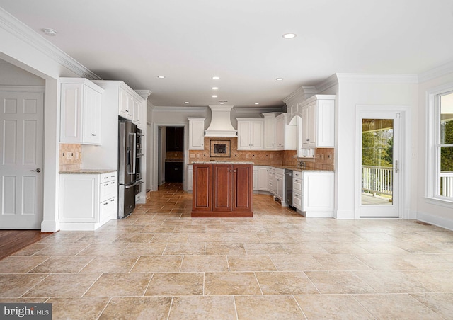 kitchen with decorative backsplash, a kitchen island, custom range hood, stainless steel appliances, and white cabinetry