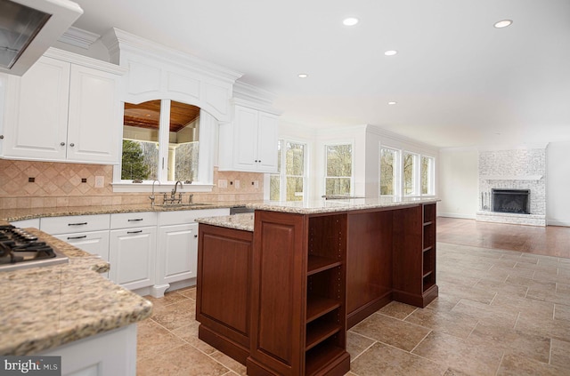 kitchen with light stone counters, a sink, a kitchen island, white cabinetry, and open shelves