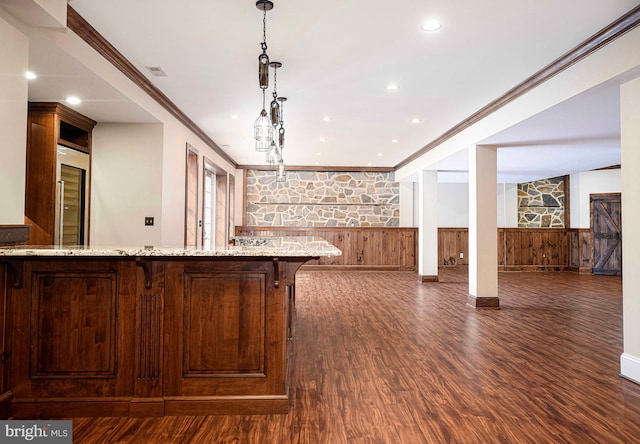 kitchen featuring a wainscoted wall, light stone counters, open floor plan, decorative light fixtures, and crown molding