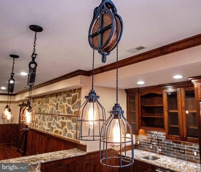 interior details with a wainscoted wall, a sink, ornamental molding, light stone countertops, and glass insert cabinets