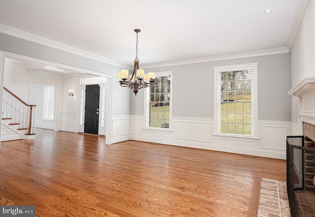 unfurnished dining area with crown molding, an inviting chandelier, a brick fireplace, wood finished floors, and stairs