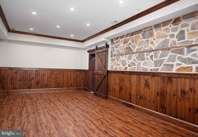 empty room with a barn door, wainscoting, wood finished floors, crown molding, and recessed lighting