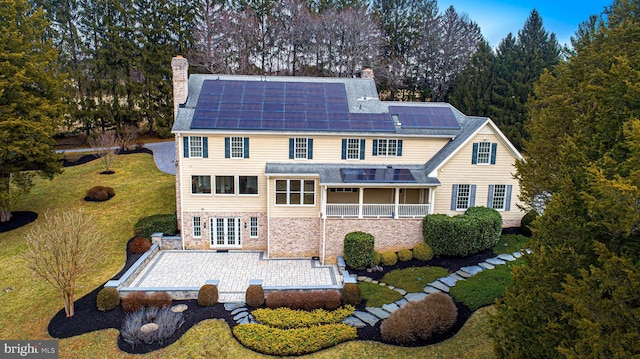 rear view of house with a patio, a yard, a chimney, and solar panels