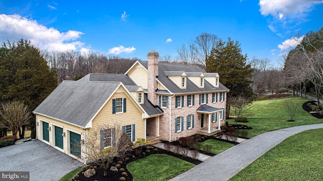 view of front facade with aphalt driveway, an attached garage, a shingled roof, a front lawn, and a chimney