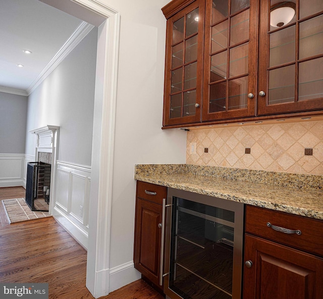 bar featuring beverage cooler, tasteful backsplash, a fireplace with flush hearth, ornamental molding, and dark wood-type flooring