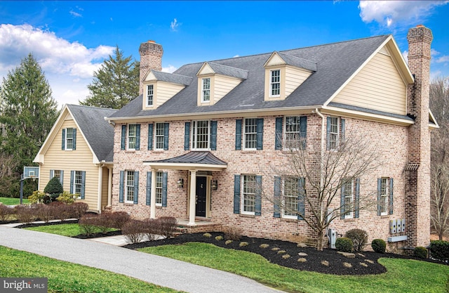 colonial home featuring roof with shingles, a chimney, a front lawn, and brick siding