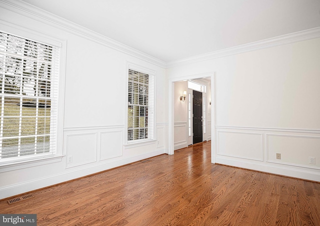 unfurnished room with visible vents, wood finished floors, and ornamental molding