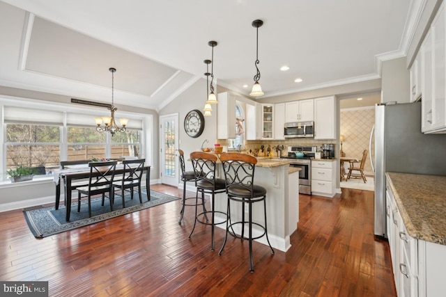 kitchen featuring light stone countertops, appliances with stainless steel finishes, white cabinets, and decorative light fixtures