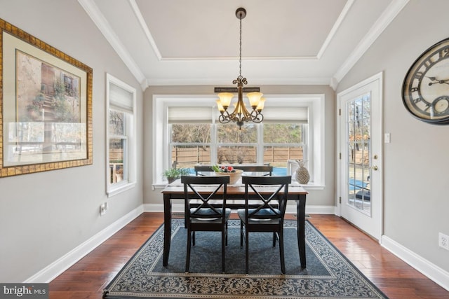 dining space featuring dark wood-type flooring, ornamental molding, a tray ceiling, and a notable chandelier