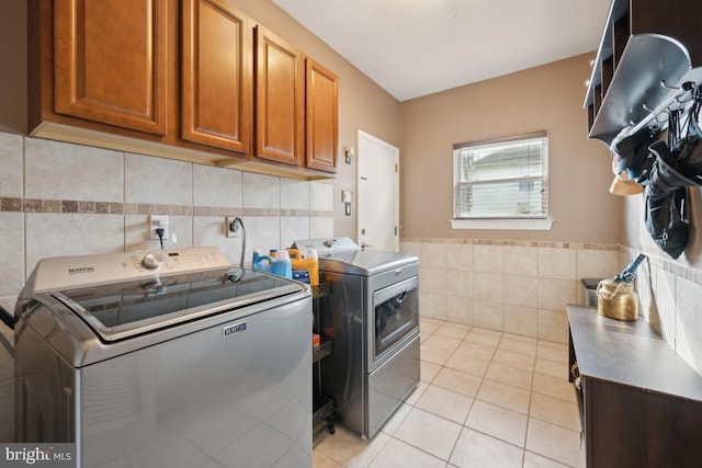 laundry area featuring light tile patterned flooring, cabinets, tile walls, and washing machine and clothes dryer