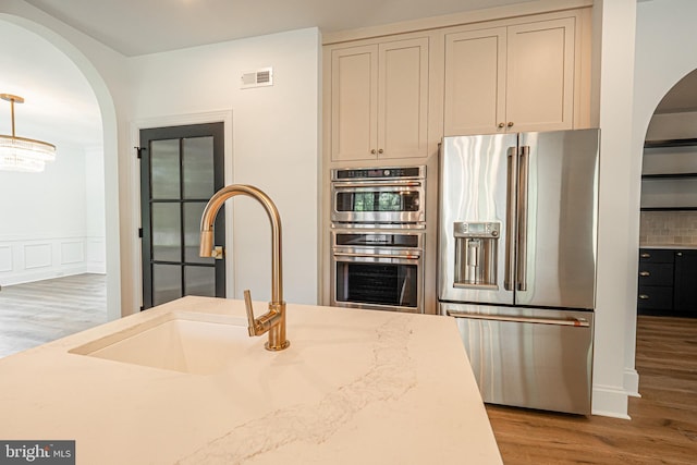 kitchen featuring pendant lighting, appliances with stainless steel finishes, sink, light wood-type flooring, and light stone counters