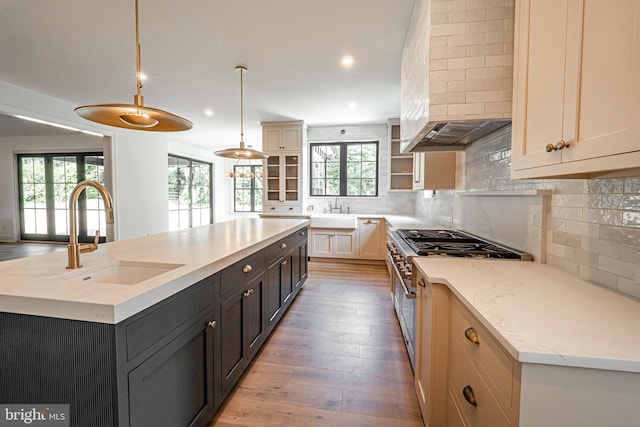 kitchen featuring a center island with sink, decorative backsplash, hanging light fixtures, light stone countertops, and sink