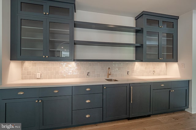 kitchen with decorative backsplash, sink, blue cabinetry, and light hardwood / wood-style floors