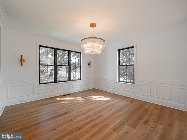 empty room with wood-type flooring, a wealth of natural light, and a chandelier