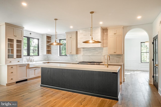 kitchen featuring pendant lighting, light hardwood / wood-style floors, sink, a center island with sink, and cream cabinetry