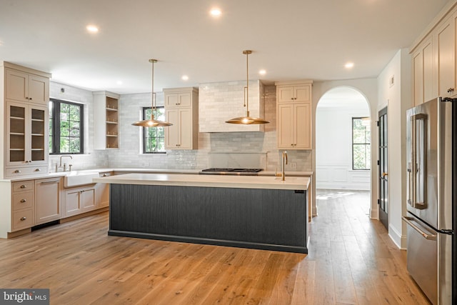 kitchen with hanging light fixtures, appliances with stainless steel finishes, a kitchen island with sink, and cream cabinets