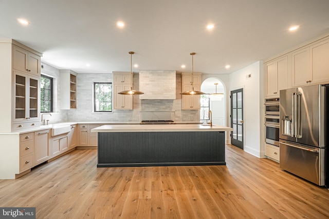 kitchen with stainless steel appliances, decorative light fixtures, wall chimney range hood, a kitchen island, and sink