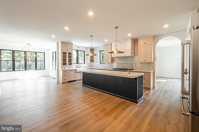 kitchen with decorative light fixtures, a center island with sink, high end fridge, and light hardwood / wood-style flooring