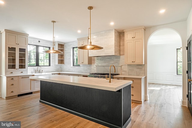 kitchen with decorative light fixtures, wall chimney range hood, light hardwood / wood-style floors, and a center island with sink