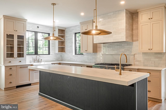 kitchen featuring decorative light fixtures, tasteful backsplash, sink, a kitchen island with sink, and light wood-type flooring