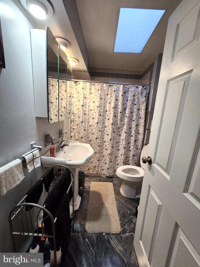 bathroom featuring sink, curtained shower, a skylight, and toilet